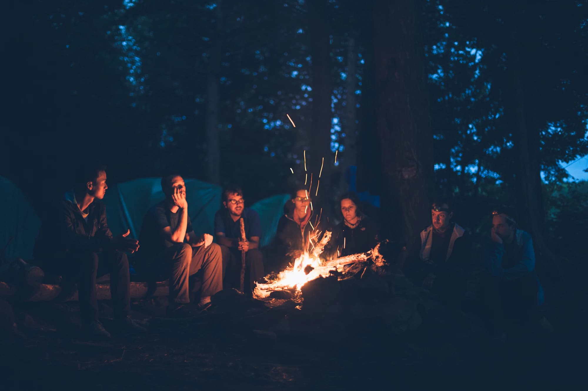 Campfire burning beside camp as night settles in